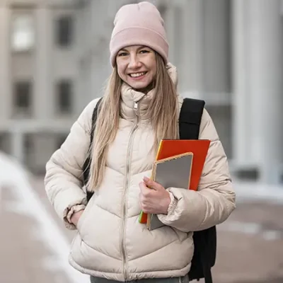 Joven estudiante sonriente con libros en la mano y ropa de abrigo
