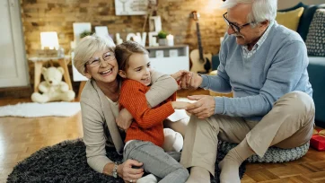 Pareja de ancianos en el salón de su casa jugando con su nieta